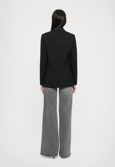 Black blazer with sharp lapels, tailored fit, and double-button closure, paired with wide-leg gray denim pants featuring a frayed hem.