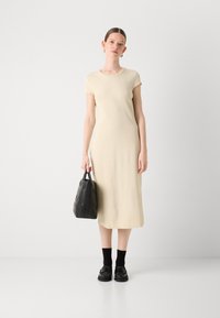 Cream-colored, knee-length dress with short sleeves, paired with a black textured handbag and black socks with loafers.