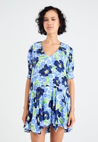 Bloemrijke jurk met een V-halslijn, korte pofmouwen en een uitlopende rok. Kleuren omvatten blauw, groen en donkere bloemmotieven op een lichte achtergrond.