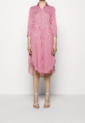 Femme portant une robe chemise midi rayée verticalement rouge et blanche, manches 3/4, et des sandales à talons hauts blanches à lanières.