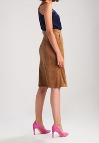 Falda midi de ante marrón con cintura ajustada y forma en A, combinada con una camiseta de tirantes azul marino y tacones altos de color rosa brillante.