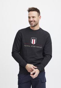 Felpa nera in misto cotone con scollatura rotonda. Presenta un logo ricamato in rosso, bianco e oro. Tessuto morbido, maniche lunghe.