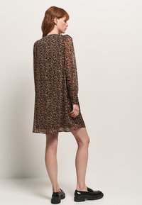 Vestido de tela sheer con estampado de leopardo, mangas largas, escote redondo y un corte relajado, combinado con zapatos planos negros.