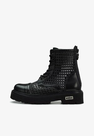 Stivali neri alla caviglia con tomaia in rete intrecciata, accenti in pelle, punta rotonda e suola spessa. Presentano una cerniera laterale e lacci nella parte anteriore.