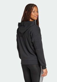 Svart hoodie gjord av en blandning av bomull, med en framficka, huva och avslappnad passform. Bärs med glansiga svarta leggings med ränder.