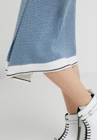 Blå stickad klänning med en vit ribbad nederkant, med svarta detaljer. Matchad med vita ankelstövlar med dragkedja och snörningsdetaljer.