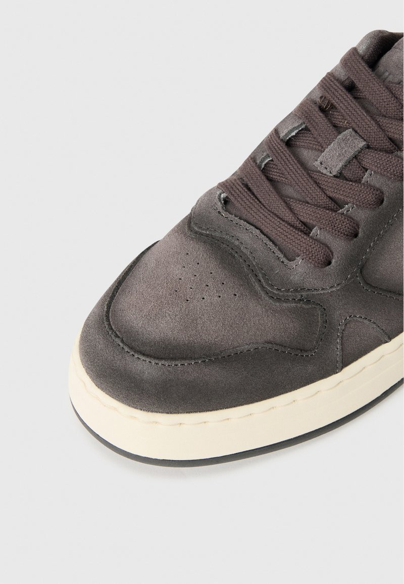 Grijze suède sneaker met een ronde neus, textuur oppervlak, platte veters en een crèmekleurige rubberen zool. Heeft kleine perforaties op de neus.
