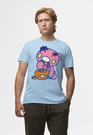 Ung mand med lyst hår iført en lyseblå T-shirt med en tegneserie af en pink bjørn, der spiser fra en udskåret orange græskar.