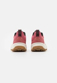 Baskets de sport roses avec une tige en maille, des accents noirs, une semelle blanche rembourrée et une semelle extérieure en caoutchouc marron, arborant un logo au niveau du talon.