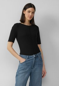 Zwarte geribbelde body met korte mouwen, ronde halslijn en gegolfde randen; gecombineerd met lichtblauwe high-waisted denim jeans.