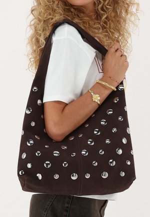Braune Wildleder-Totebag mit großen silbernen runden Akzenten und Aussparungen. Weiche Textur, breiter Schulterriemen und offenes Design.