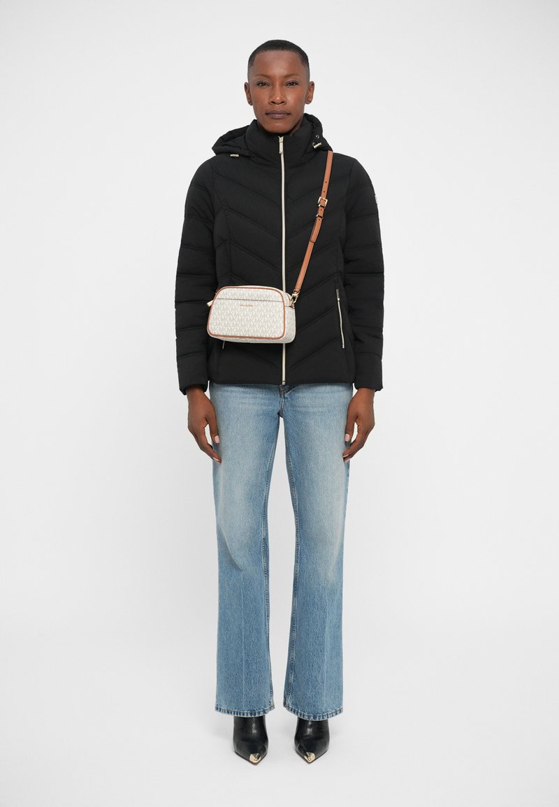 Veste noire matelassée avec capuche, jeans large bleu clair, et un sac bandoulière crème avec un motif géométrique et une sangle marron.