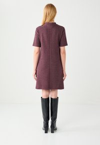 Bordowa sukienka z krótkim rękawem o prostym kroju, z tylnym zamkiem błyskawicznym i subtelną teksturą, zestawiona z czarnymi połyskującymi kozakami za kolano.