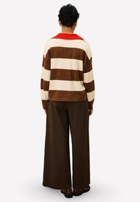 Gestreepte trui in crème en bruin met een rode kraag, gecombineerd met losse bruine broek, gezien vanaf de achterkant. Gelaagd gebreid materiaal.