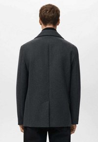 Abrigo gris a medida con solapa con muesca, hombros estructurados y tejido texturizado. Cuenta con una abertura trasera y bolsillos laterales.