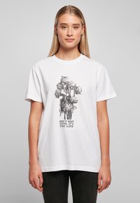 Hvitt bomull T-skjorte med et svart-hvitt blomster grafisk design med teksten "VENT IKKE TIL DET ER FOR SENT" under. Korte ermer.