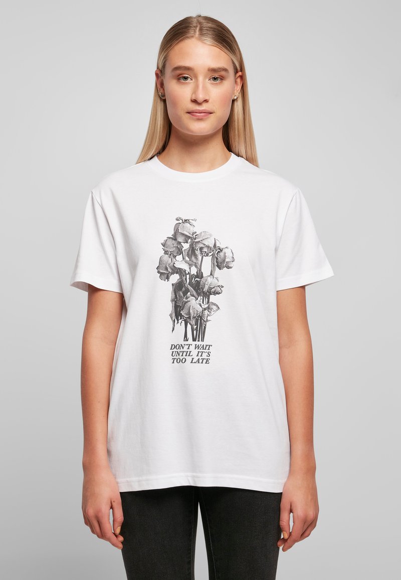 Hvitt bomull T-skjorte med et svart-hvitt blomster grafisk design med teksten "VENT IKKE TIL DET ER FOR SENT" under. Korte ermer.