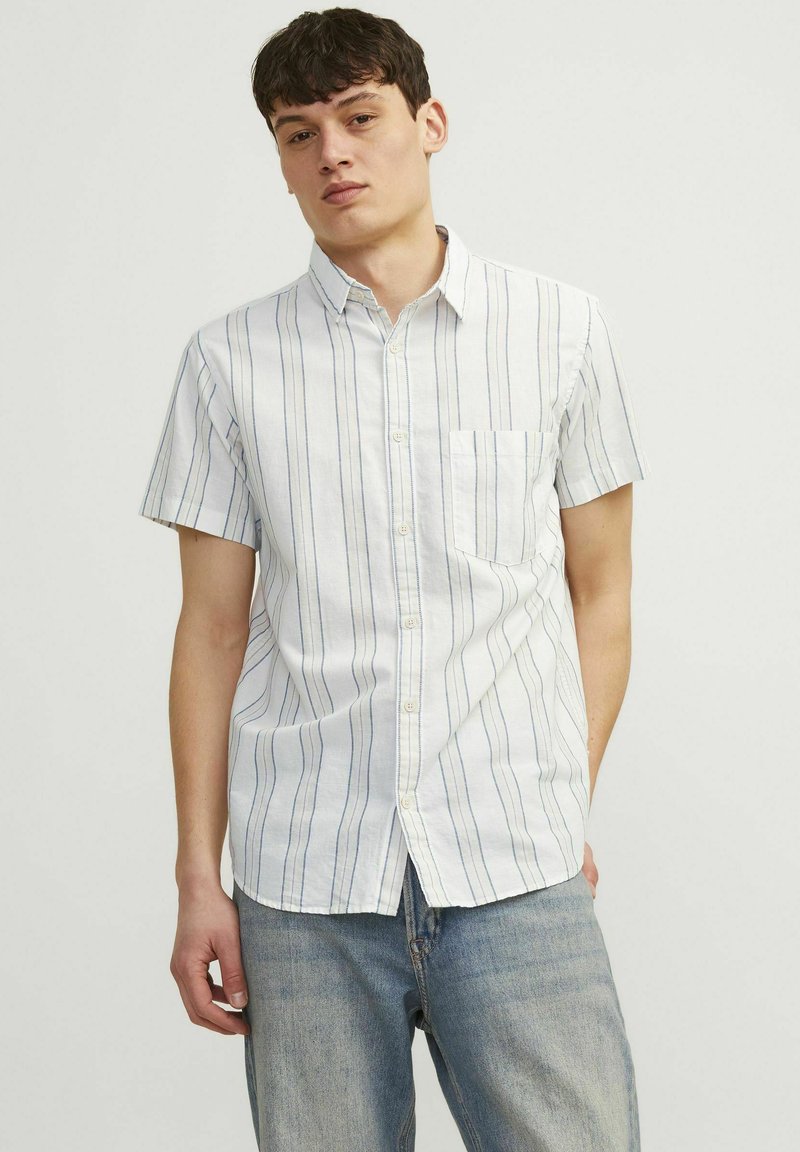 Camisa de botones de manga corta en tejido ligero. Blanca con rayas azules verticales. Cuenta con un bolsillo en el pecho y un cuello estándar.