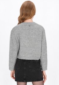 Szary, puszysty sweter z okrągłym dekoltem i długimi rękawami, zestawiony z czarną dżinsową mini spódnicą z tylnymi kieszeniami.