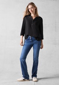 Sort langærmet bluse med knaplukning og V-udskæring, parret med blå denim flared jeans og hvide sneakers med sorte accenter.