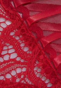 Tissu en dentelle rouge avec des motifs complexes, featuring des rubans en satin lisses tissés à travers. La texture est délicate et légèrement transparente.