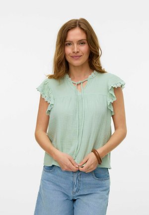 Light green, textured top with ruffled short sleeves and a keyhole neckline. Paired with blue denim jeans. Simple and breathable design.