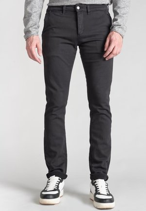 Vaqueros negros slim-fit con una textura suave, que presentan una cremallera y lazos para el cinturón, combinados con zapatillas negras y blancas.