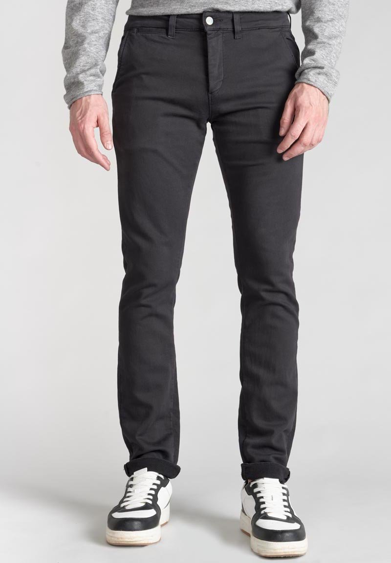Jeans neri slim fit con una texture liscia, dotati di zip e passanti per cintura, abbinati a sneakers bianche e nere.