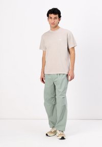 Lichtbeige t-shirt met een klein wit logo, gecombineerd met losse, mintgroene broeken en beige sneakers. Eenvoudig ontwerp en comfortabele pasvorm.