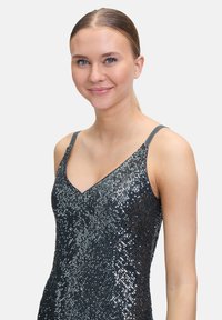 Sukienka bez rękawów z dekoltem w serek, wykonana z materiału wyszywanego cekinami w różnych odcieniach szarości, tworząca teksturowany, błyszczący wygląd.