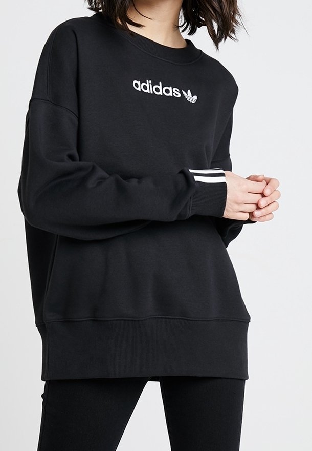 Černá mikina s bílým logem Adidas, kulatý véčkový výstřih, spadlé ramena a žebrované manžety s bílými pruhy. Bavlněný materiál, volný střih.