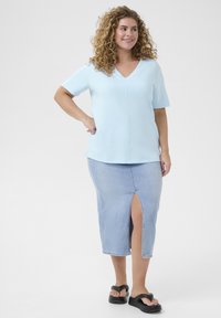Lichtblauwe top met korte mouwen en een V-hals, gecombineerd met een denim rok met een voorknip. Zwarte platformsandalen maken de look af.