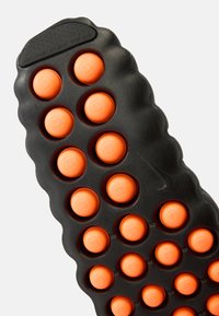 Μαύρη λαστιχένια σόλα με πορτοκαλί κυκλικά στοιχεία, που διαθέτει υφασμένο κυματιστό σχέδιο και μικρές τετράγωνες λεπτομέρειες σε κάθε κουμπί.