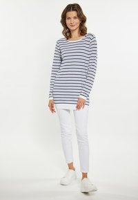 Maglietta a maniche lunghe a righe blu e bianche con scollatura ampia, abbinata a pantaloni bianchi attillati e sneakers bianche.