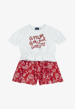 Top bianco a maniche corte con la scritta “amor” in caratteri rossi e un fiore, abbinato a pantaloncini rossi con motivi floreali bianchi.