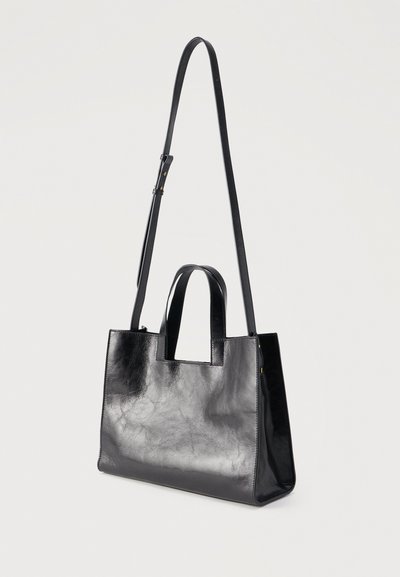 Μαύρη δερμάτινη τσάντα χειρός σε ορθογώνιο σχήμα με δύο κοντές λαβές και έναν μακρύ ρυθμιζόμενο ιμάντα ώμου, πάνω σε απλό φόντο.