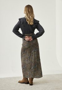 Blusa oscura de manga larga con hombros con volantes que contrasta con una falda larga de estampado, que presenta colores terrenales y motivos de hojas. Botas marrones hasta el tobillo completan el conjunto.