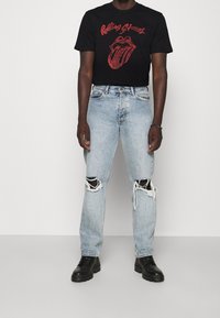 Czarna koszulka z czerwonym logo "Rolling Stones", w połączeniu z jasnoniebieskimi, zniszczonymi dżinsami z przetarciami na kolanach oraz czarnymi botkami do kostki.