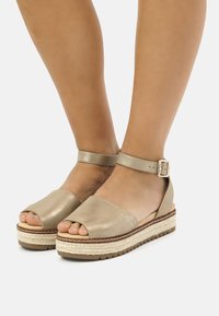 Sandalias de plataforma beige con punta abierta y tira en el tobillo, que cuentan con una entresuela de yute trenzado y un acabado de cuero suave. Detalle de hebilla ajustable.
