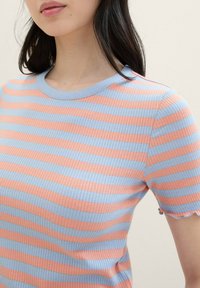 Camiseta de canalé en rosa y azul claro con rayas horizontales, con un cuello redondo y bordes de las mangas en ondas. Textura de tela suave.