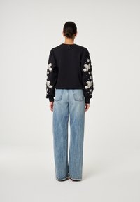 Zwarte cropped sweatshirt met geborduurde witte bloemenpatronen op de mouwen, gecombineerd met lichtblauwe high-waisted wijde jeans.