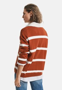 Pull rayé en orange brûlé et blanc, avec un col et des poignets côtelés. Superposé sur une chemise blanche à rayures, avec une coupe décontractée.
