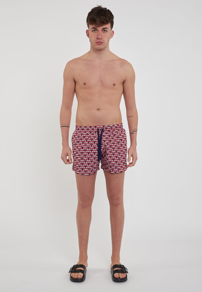 Costumi da bagno con un motivo geometrico rosso e bianco su uno sfondo blu navy, con una vita regolabile e tasche laterali.