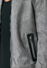 Veste bomber en cuir suédé gris avec une finition texturée, dotée d'une poche zippée noire sur la manche et d'un zip avant argenté.