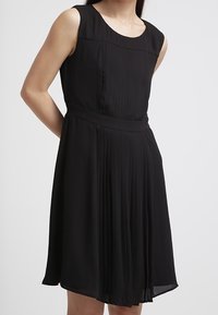 Vestito nero senza maniche con gonna plissettata, vita aderente e scollatura tonda. Realizzato in tessuto leggero con una trama liscia.