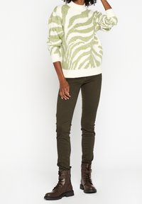 Suéter de punto con un patrón de cebra en verde y blanco, combinado con pantalones ajustados verde oliva y botas de tobillo marrones con cordones.