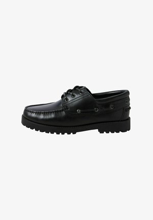 Schwarzer Leder-Bootsschuh mit Schnürung vorne, Moc-Toe-Naht, Metallösen und dicker Gummisohle, von der Seite vor weißem Hintergrund gezeigt.