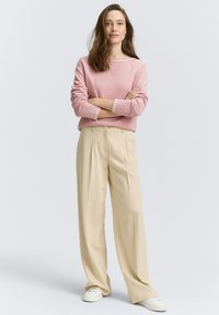 Maglione a righe rosa chiaro con maniche lunghe, abbinato a pantaloni beige a vita alta, caratterizzati da una vestibilità comoda e sneakers bianche.