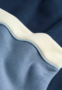 Tissu superposé mettant en valeur des nuances de bleu et de crème, avec une texture lisse, des coutures courbes et des motifs contrastants.