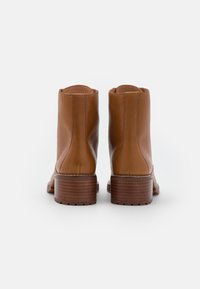 Brązowe skórzane botki za kostkę o gładkiej fakturze, zaokrąglonym nosku i drewnianym, warstwowym obcasie. Charakteryzują się minimalnym przeszyciem i brakiem widocznych elementów metalowych.